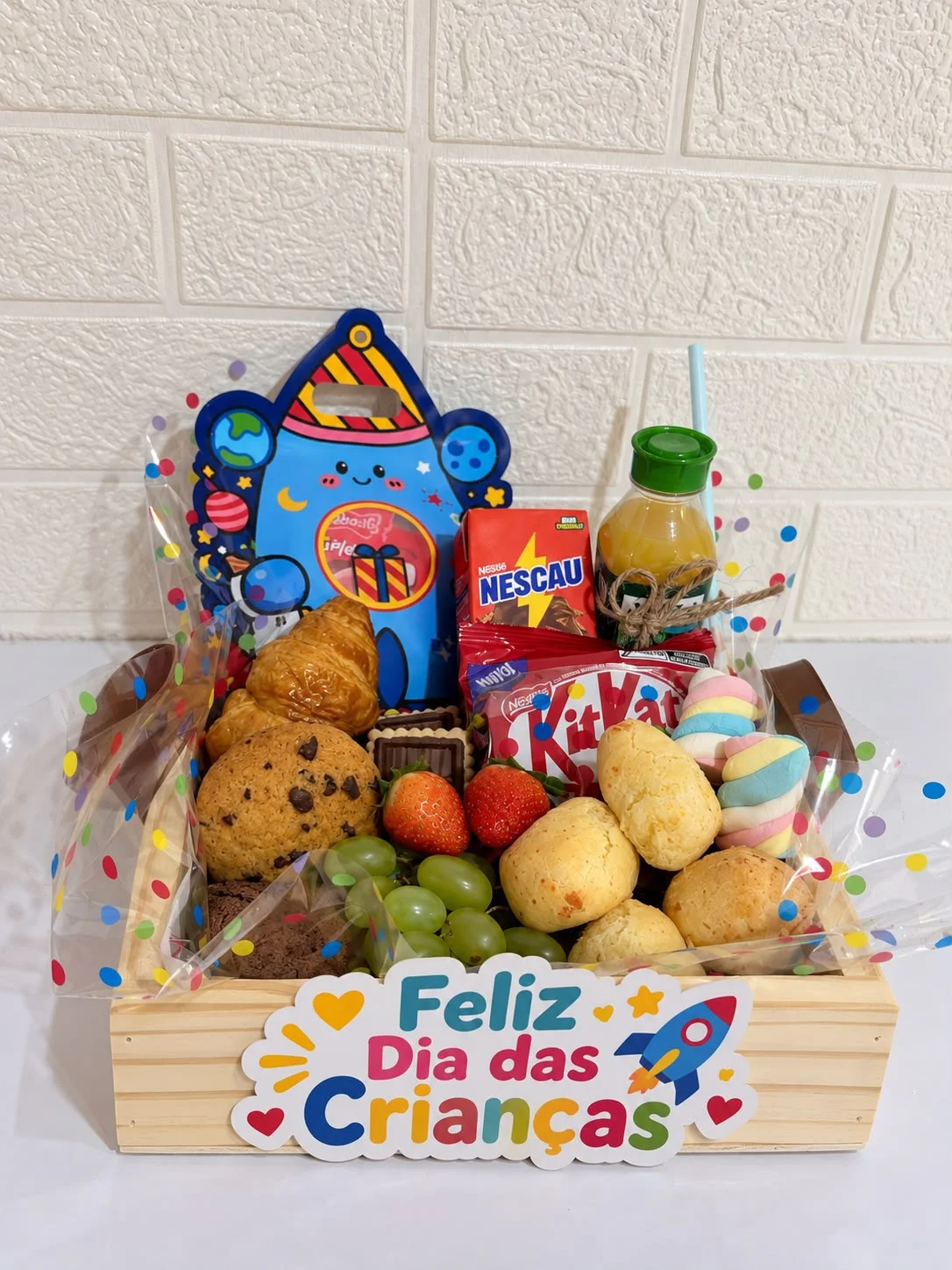 Box Dia das Crianças com guloseimas, frutas, croissant, pão de queijo, suco e achocolatado, visto de frente